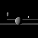 Rhea seen in front of Saturn’s rings. The moons Dione, left, and Enceladus, right, are in the background.